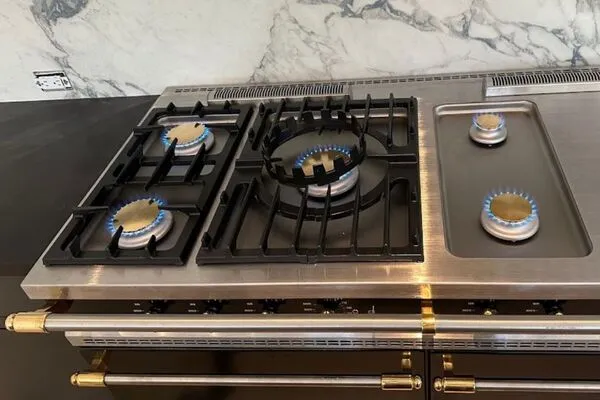 A close-up shot of a black and stainless steel gas range with two burners and a griddle lit with blue flames.