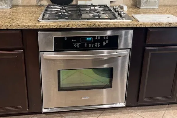 A built-in stainless steel microwave oven and a gas stovetop on a granite countertop, with dark wooden cabinets.