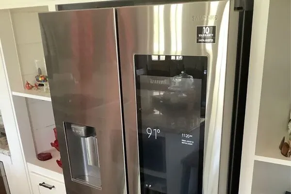 A stainless steel Samsung smart refrigerator with a digital screen on the door displaying the temperature and time.
