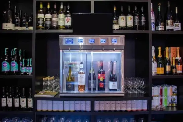 A commercial wine cooler and display unit filled with multiple bottles, surrounded by shelves stocked with various wines and beverages.